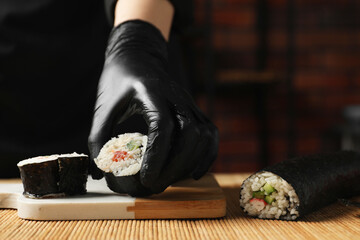 Chef in gloves putting sushi roll onto board at table, closeup