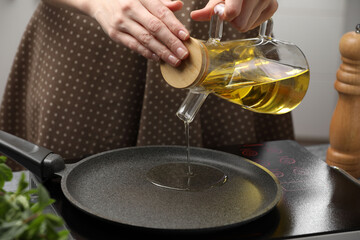 Vegetable fats. Woman pouring cooking oil into frying pan on stove in kitchen, closeup