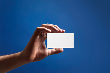 Man with blank business card on blue background, closeup. Mockup for design