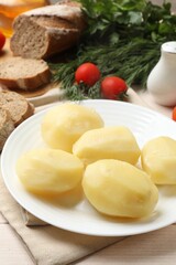 Plate with young boiled potatoes on light wooden table, closeup