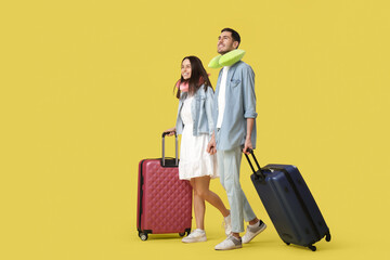 Beautiful young happy couple of tourists with suitcases and travel pillows on yellow background