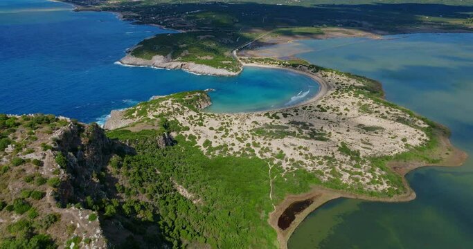 Capture of the stunning curved sandy shoreline and clear blue waters of Voidokilia Beach in Greece, surrounded by lush greenery and rocky formations.