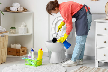Young woman cleaning toilet bowl in modern bathroom