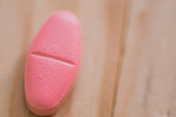 Closeup of pink tablet on brown blurred background.