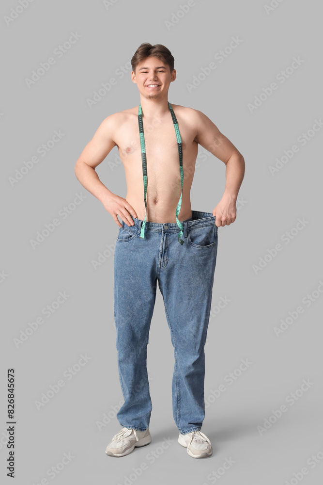 Poster sporty young man in loose jeans and with measuring tape on grey background. diet concept