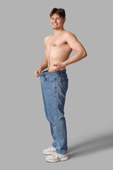 Fototapeta premium Sporty young man in loose jeans on grey background. Diet concept