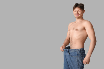 Sporty young man in loose jeans on grey background. Diet concept