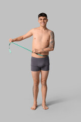 Fototapeta premium Smiling young man measuring waist with tape measure, weight loss and fitness progress, healthy lifestyle