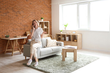 Young pretty woman sitting on sofa and talking with mobile phone on sofa in living room