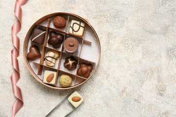 Box with delicious chocolate candies and kitchen tongs on light background