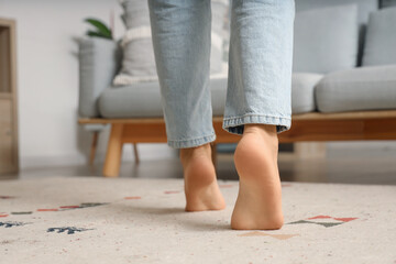 Barefoot woman walking on carpet at home, back view