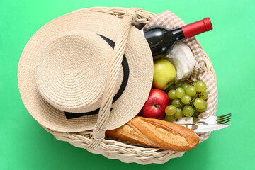 Tasty food and drink in wicker basket for picnic on green background. Top view