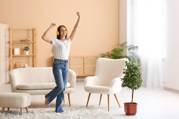 Young happy woman in headphones dancing in living room