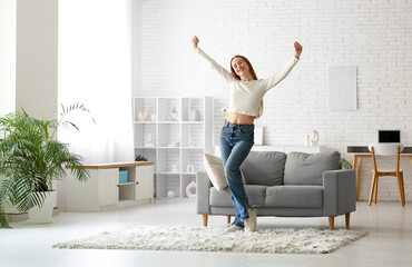 Young woman dancing near sofa in living room