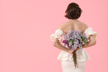 Young woman with bouquet of blooming lilac flowers on pink background, back view