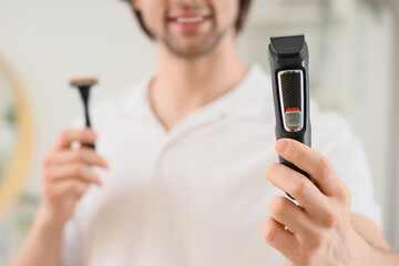 Young man with trimmer and razor in bathroom, closeup