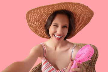 Young woman taking selfie with small  electric fan on pink background