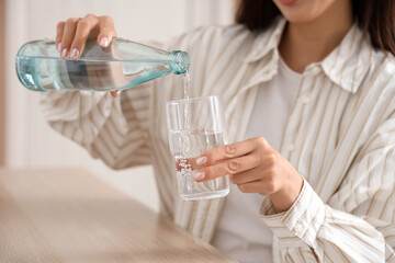 Young woman pouring water into glass at table in office, closeup