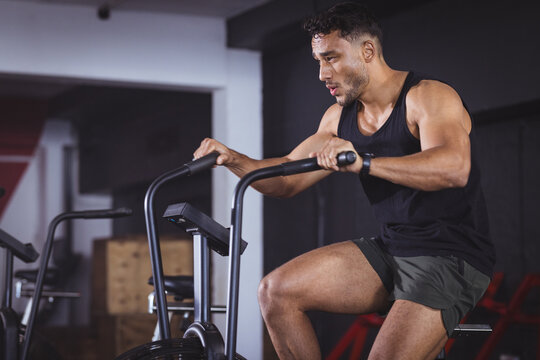 At gym, biracial man working out on stationary bike, looking strong and fit
