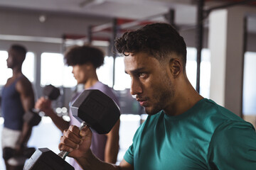 At gym, diverse men lifting dumbbells, looking focused and fit in gym background