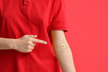 Female blood donor pointing at applied patch on red background, closeup