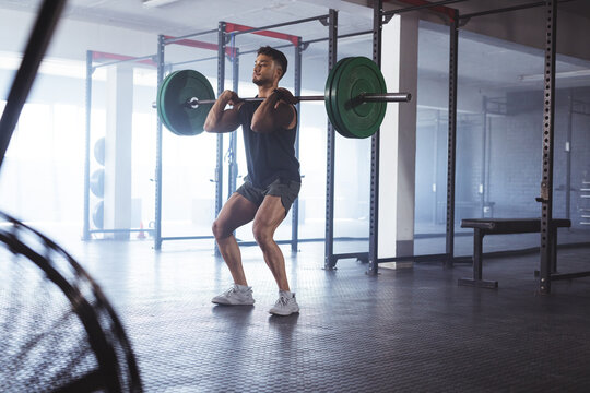 Young biracial man lifting weights at gym, looking strong and fit