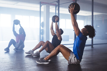 Three young, fit, diverse men working out with medicine balls at gym