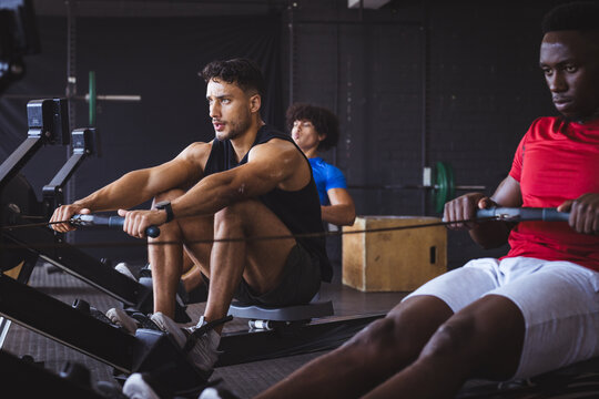 At gym, three young diverse men working out on rowing machines