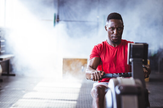 At gym, African American man working out on rowing machine, focused and determined, copy space
