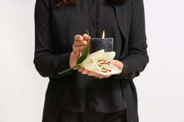 Young woman with funeral bouquet of lily flowers and burning candle on white background, closeup