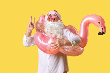 Santa Claus with swim ring showing victory gesture on yellow background. Christmas in July
