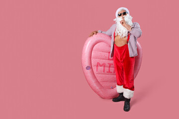 Santa Claus with swim mattress showing silence gesture on pink background. Christmas in July