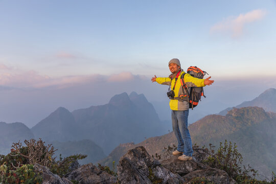 Cheerful smiling male photographer with dslr camera on top hills raised hands