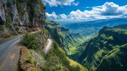 A dramatic mountain road with sharp cliff drops on one side and lush green valleys on the other,...