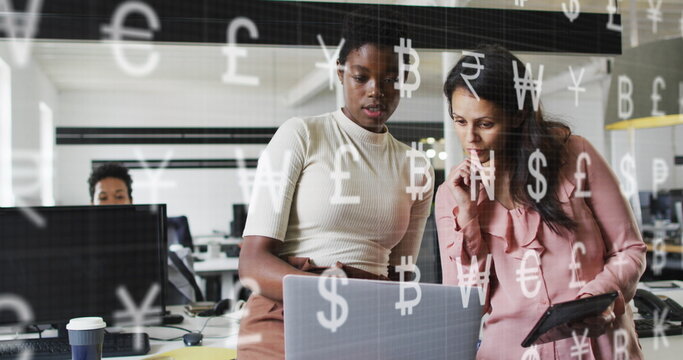 Image of currency symbols against two diverse women discussing at office