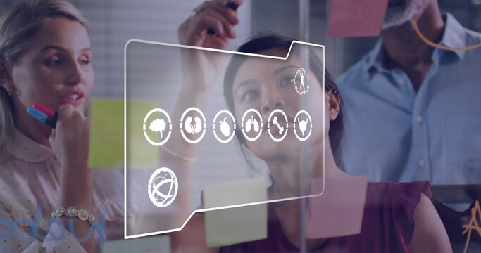 Image of multiple digital icons against diverse colleagues discussing over memo notes at office