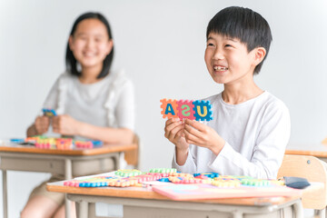 学校の教室でアルファベットのおもちゃを使って英語を勉強する小学生の男の子（低学年）
