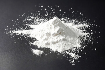 A pile of white powder sits on a black background. The powder is scattered around the pile, creating a textured look. The image is perfect for illustrating concepts of cleanliness, purity, or freshnes
