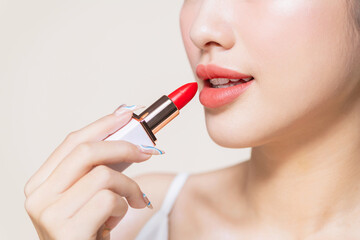 pretty asian woman using a red lipstick on beige background