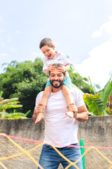 Dad carries his young son on his back, both smiling and enjoying playful moments. The image...