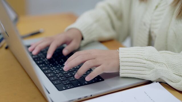 A woman is typing on a laptop with her hand on the keyboard. She is wearing a white sweater and she is focused on her work