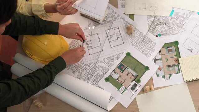 Architect and safety engineer discussion about building construction use blueprint on table with architectural document, measurement tool and wooden block scatter around at modern office. Delineation.