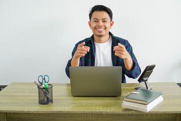 young asian freelancer sitting in workplace smiling pointing to the front