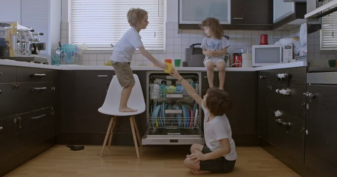 Three kids in casual attire collaboratively load dishes into a dishwasher, fostering teamwork and cooperation, in a contemporary kitchen.
