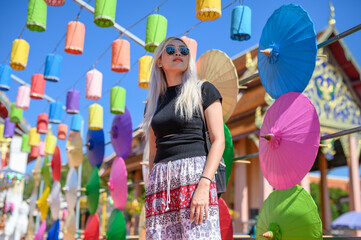  a young woman standing among an array of colorful lanterns and umbrellas. The bright, sunny sky...