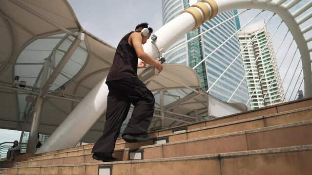 Asian hipster wear headphone listen hip hop style and moving to music. Professional young break dancer walking or step up stairs while dancing with low angle camera. Outdoor sport 2024. Sprightly.