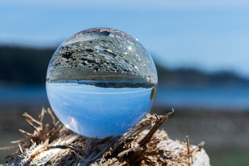 An image of a large photographic lens ball reflecting an inverted image of a rocky coastal shoreline. 