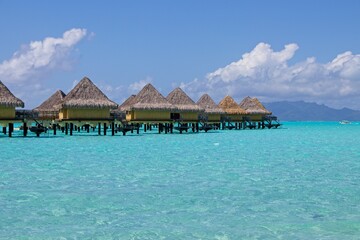 Overwater bungalows of the Intercontinental Le Moana sit over crystal clear, warm, pastel-colored waters of Bora Bora