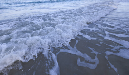 A pristine beach with turquoise waters, foamy waves, and a soft sandy shore under a blue sky with fluffy clouds.