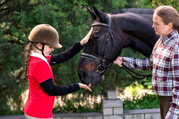 Young rider pets horse with instructor's supervision.